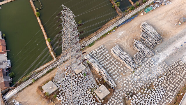 Aerial view of a high-voltage electricity pylon surrounded by numerous concrete tetrapods near water in Semarang, Central Java, Indonesia.