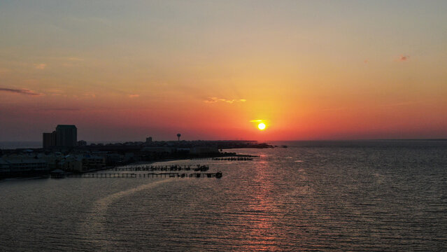 Aerial view of the sunset over the coastline with buildings, piers, and calm water in Navarre Beach, Florida, United States.