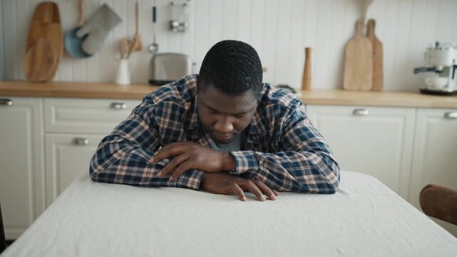 Adult african male person stay at home alone and bored, portrait in kitchen. Depression and frustration of modern people, loss of interest or pleasure in normal activities, emptiness or hopelessness