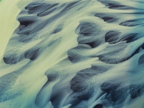 Aerial view of abstract snow and ice patterns on the slopes of Naustavik Mountain, with intricate textures and shadows in the rugged landscape of Husavik, Nordurthing, Iceland.