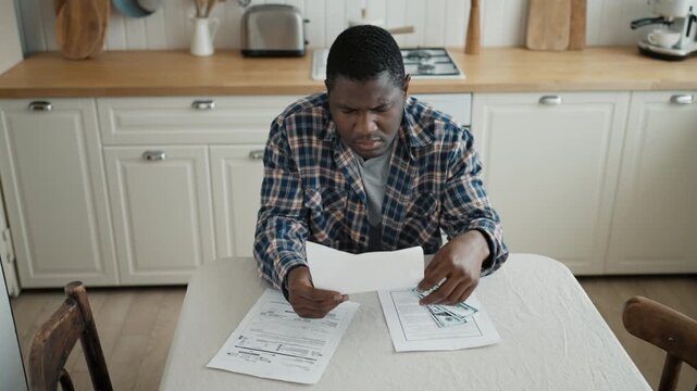 Lack of money and debts, black man viewing bills and counting money at home. Depression of poverty and jobless, financial troubles of african immigrants, overdue mortgage payments, portrait indoors