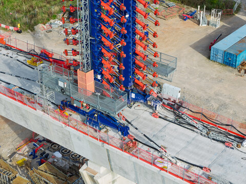Aerial view of High Speed Rail Construction featuring a large blue and red launching gantry machine placing concrete bridge segments on a viaduct in the United Kingdom.