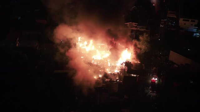 Philippines, Palawan, Puerto Princesa 10.05.2026: Close overhead aerial night view of house frames burning in Barangay Masipag, with intense flames, billowing smoke and emergency vehicles beside.