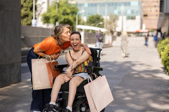 Mother kissing adult daughter in wheelchair after shopping