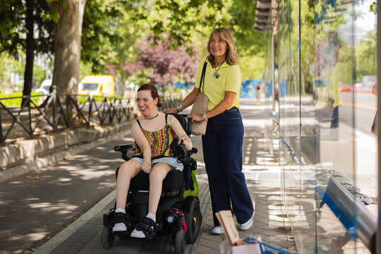 Woman in electric wheelchair smiling with friend at bus stop