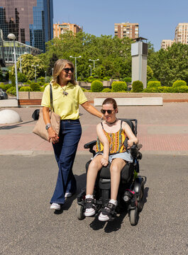 Woman helping young woman in electric wheelchair outdoors
