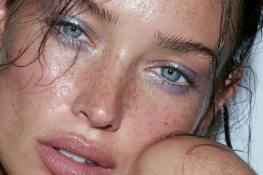 Woman's close-up portrait with wet skin, freckles, and iridescent eye makeup
