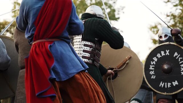 Viking warriors in full armor practicing combat drills with shields outdoors.