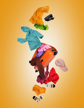 Levitation of open orange suitcase with colorful apparel and accessories floating in the air on yellow background
