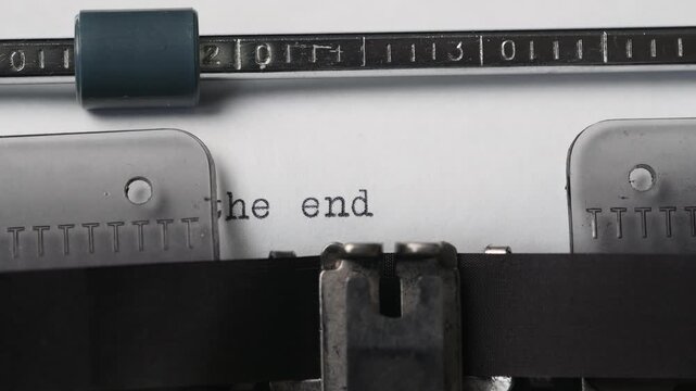 Typewriter shows the words 'the end' on a sheet of paper in a home office setting during the day
