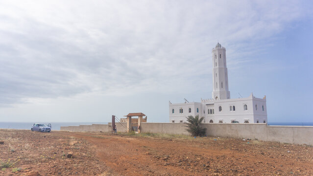 Historic white lighthouse tower situated on a rocky coastal cliff with building