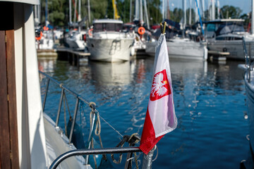 Polska bandera żeglarska z godłem zamontowana na relingu jachtu w porcie z widokiem na marinę © Kamil_k2p