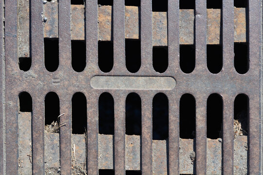Full frame background texture of a weathered cast iron storm drainage grate featuring parallel vertical slots and a textured metallic surface with rust spots.