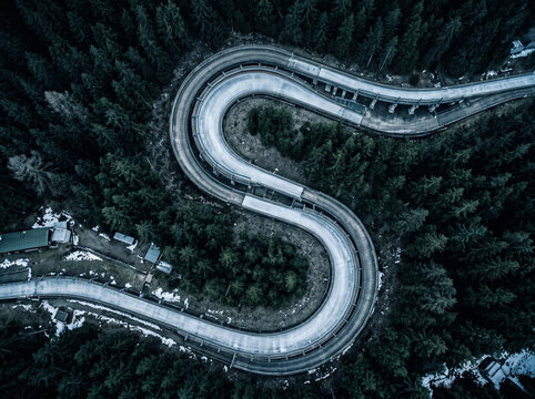 top view of winding bobsled track in snowy coniferous forest bends of ice chute from drone aerial