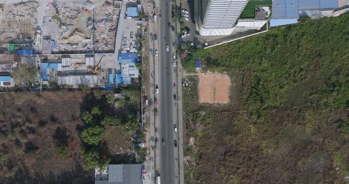 Aerial top down view captures a busy urban road separating an active construction site from a high-rise building and a patch of green, undeveloped land.