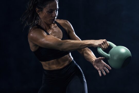 Athletic woman swinging a kettlebell during strength training. Kettlebell exercises in gym. Functional fitness and weight training. Athletic conditioning, power and endurance.