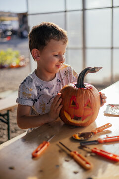 Cute kid carving and painting a spooky halloween pumpkin. Arts and crafts theme. 