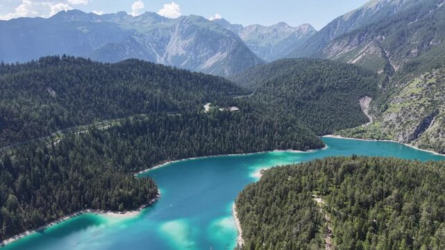 Aerial view overlooks bright turquoise shallows merging into deeper blue Blindsee between forested shores in the Austrian Tyrol for calming nature films and alpine travel campaigns