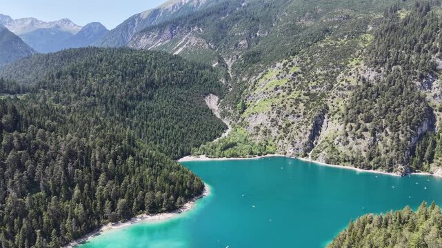 Aerial view shows turquoise Blindsee tucked beneath a steep rocky mountain wall and forested slopes in the Austrian Tyrol for tranquil alpine tourism and wilderness storytelling