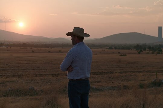Man in straw hat looking at sunset over dry field