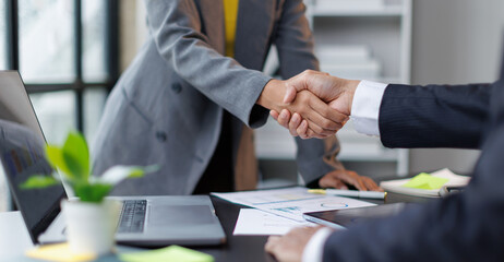 Fototapeta na wymiar Business professionals shaking hands across a desk with documents and a laptop, signifying a successful agreement, partnership, and trust in a corporate environment