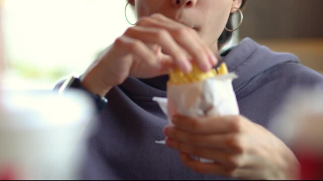 Teenage girl with striking colorful hair shares a casual dining moment with French fries in a fast-food cafe, highlighting individuality, youthful style, and carefree enjoyment.