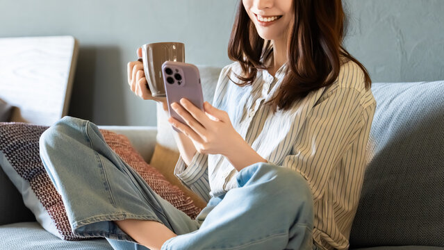 リビングのソファに座ってスマートフォンを使う女性