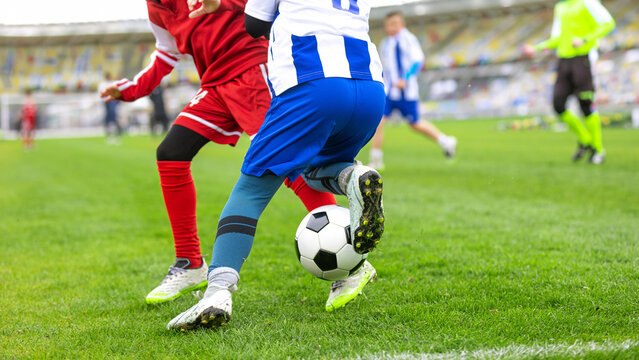 Football Dribbling Between Youth Players. Kids in a Soccer Game. Close-Up Action Shot of Junior Soccer Player in Blue Striped Kit Dribbling Soccer Ball Past Opponent in Red Kit During Match