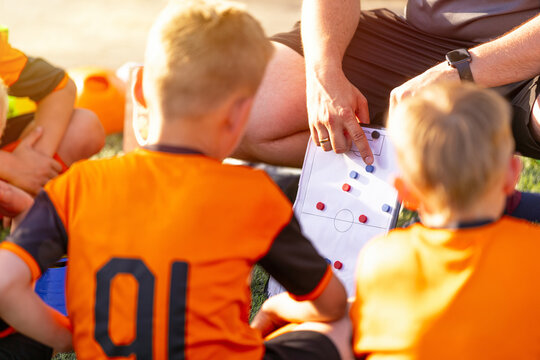 Coaching Children in Football Soccer. Youth Soccer Coach Holding Tactical Board Showing Strategy to Junior Player in Orange Jersey Number 10 During Team Meeting