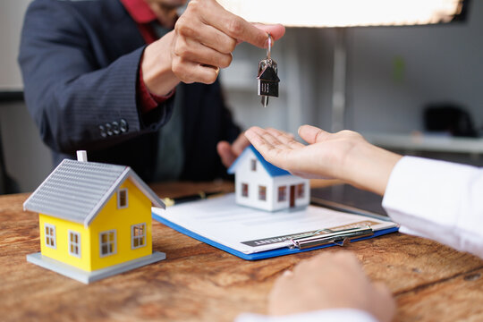 Real estate agent handing over house keys to a client, symbolizing a successful property deal, mortgage approval, and home ownership transfer after signing important financial documents