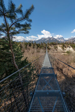 A long suspension bridge leading through Pfynwald forest towards mountains in Valais, Switzerland