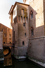 Castello estense fortress showing brick walls, corner tower, and reflective moat water © Marino Bocelli