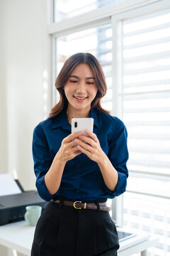 Happy busy young business woman using mobile phone, sitting at table in workplace, chatting , using app, enjoying online communication
