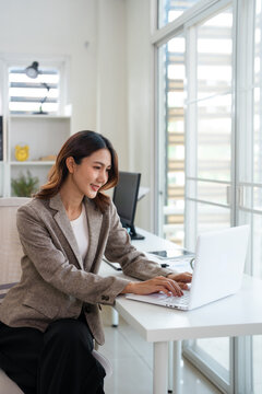 Young and happy asian woman working in modern office using laptop.