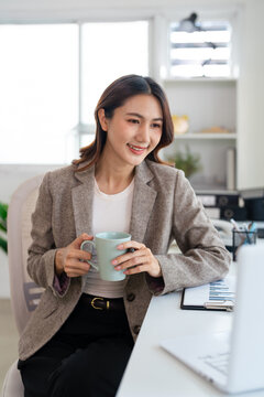 Asian woman business worker using laptop drinking coffee at office