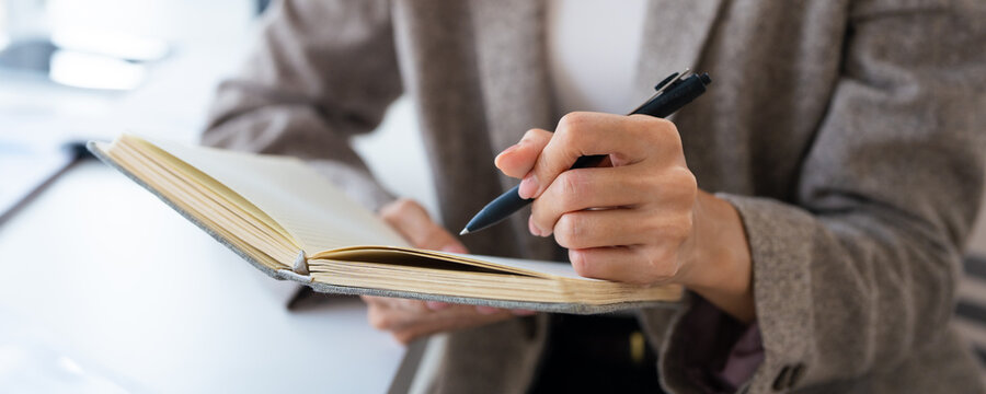 Young businesswoman hand holding pen taking notes , sitting at desk with laptop , analyzing information.
