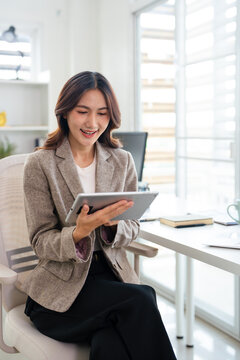 Professional business woman looking at online trade app. ASian woman holding digital tablet using fintech tab application at workplace in office.