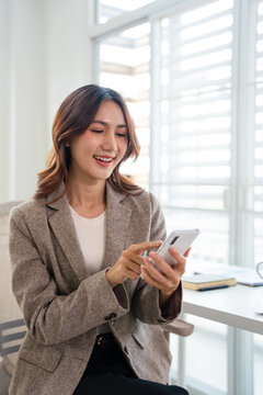 Happy busy young business woman using mobile phone, sitting at table in workplace, chatting , using app, enjoying online communication