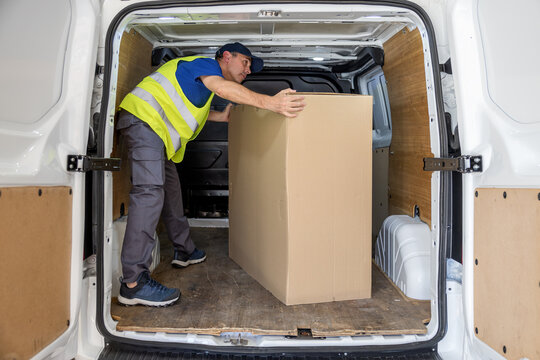 Man warehouse worker positioning large cardboard box inside cargo van