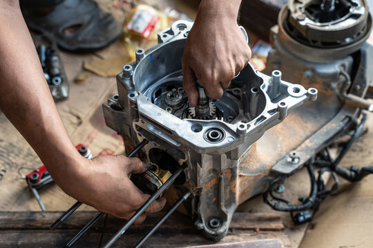 High angle close-up view of a skilled auto mechanic using hands to carefully align and install a crankshaft and piston assembly inside an aluminum motorcycle crankcase during an engine overhaul.