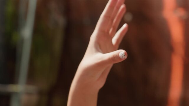 Close up of hand with white polka dot nail polish fingers moving to display manicure. background is softly blurred outdoor setting with warm lighting and natural elements like greenery