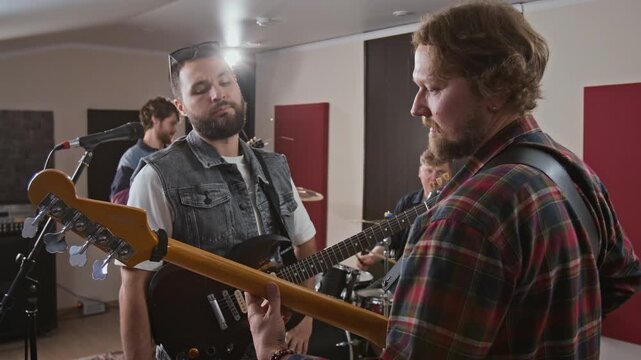 Young adult Caucasian musicians discussing chords during rock band rehearsal in sound studio. Footage perfect for music production tutorials and promotional campaigns