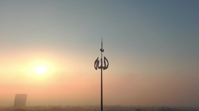 Aerial view of a spire featuring Arabic calligraphy against a golden sunset sky over the city of Malang, East Java, Indonesia.