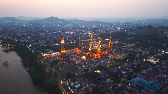 Aerial view of the illuminated Baitul Muttaqien Mosque at sunset, situated along the Mahakam River in Samarinda, East Kalimantan, Indonesia.