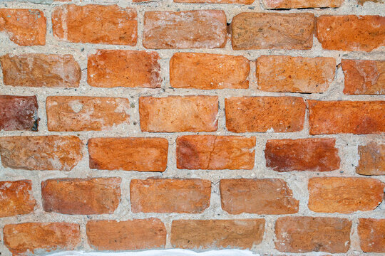 Close-up view of weathered red brick masonry with gray mortar joints showing texture and age. Terracotta brickwork in varied orange and brown tones arranged in horizontal courses with cement pointing.