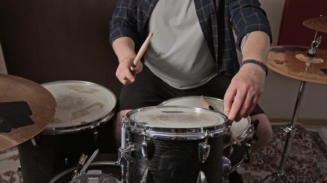 Midsection view of unknown male drummer tuning tom drumhead with drum key and drumstick. Footage suitable for music school tutorials, gear maintenance guides, and studio promos