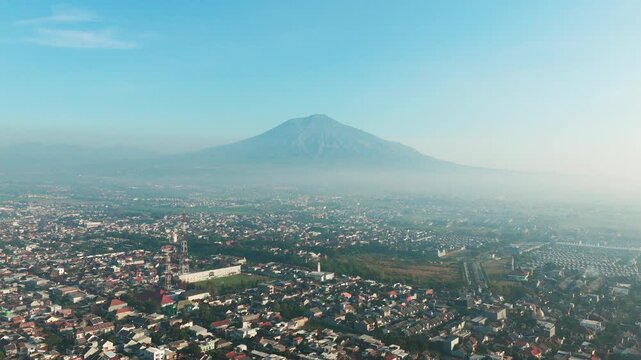 Aerial view of the city of Malang with a large mountain in the background under a clear blue sky in Malang, East Java, Indonesia.
