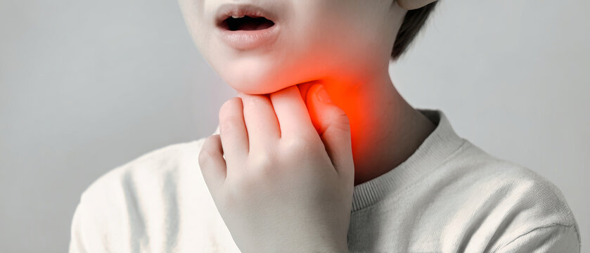 A child stands at home, touching their throat with a worried loo