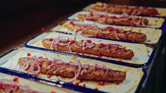 Enamel trays of grilled kebabs on lavash lined up ready for service in a Georgian restaurant.