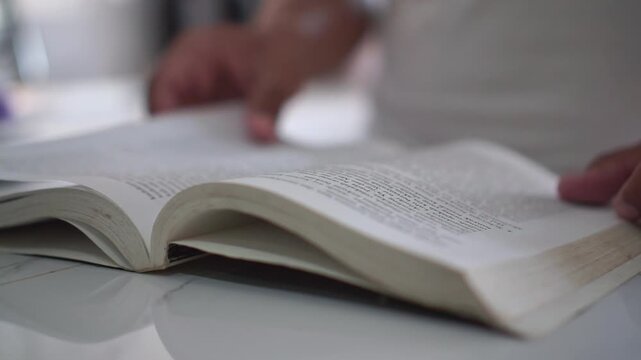 a hand paging through a book slowly and carefully. Ideal footage for education, reading, and knowledge-based content.